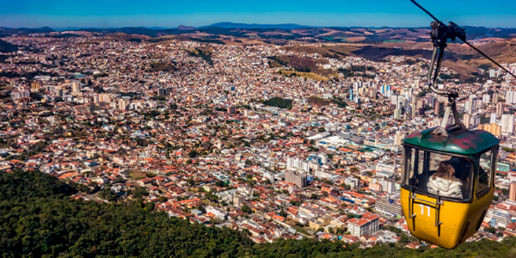 Foto com o teleférico amarelo de Poços de Caldas em destaque e a cidade ao fundo em meio às montanhas do interior de Minas Gerais